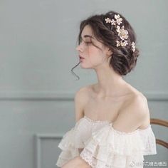 a woman wearing a white dress with flowers in her hair, sitting on a chair