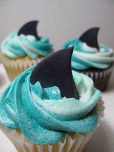 two cupcakes with blue frosting and a black shark fin on each one