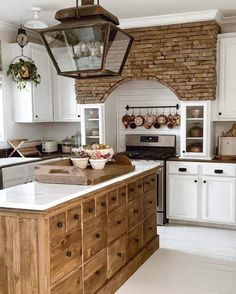 a kitchen with white cabinets and an island in front of a brick wall that has potted plants on it