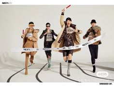 three models in trench coats and hats crossing a ribbon