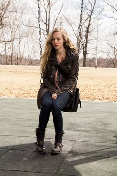 a woman is sitting on a swing in the middle of a park with her hands clasped to her knees