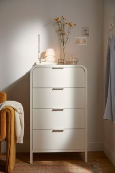 a white chest of drawers sitting next to a yellow chair in a room with light coming through the window