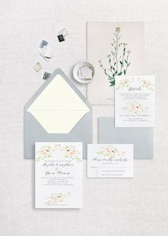 the wedding stationery is laid out on a white tablecloth with grey envelopes and matching cards