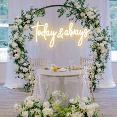 a table with white flowers and greenery under a neon sign that says today & always