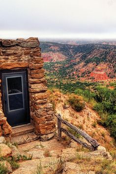 an outhouse sits on the edge of a cliff overlooking a valley and mountains in the distance