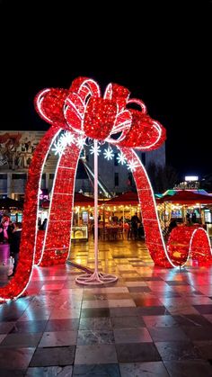 a large red bow with lights on it in the middle of a plaza at night