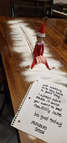 an elf sitting on top of a table next to a note