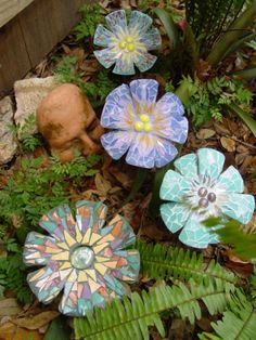 small ceramic flowers in the garden with ferns and other plants around them on the ground