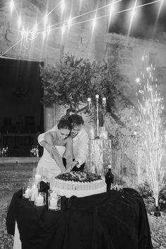 two people cutting into a cake with sparklers on the ceiling behind them and lights strung from above