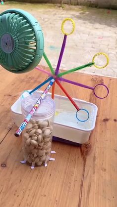 a plastic container filled with lots of different colored straws next to a fan on top of a wooden table