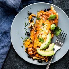 a plate with an enchilada and avocado on it next to a fork