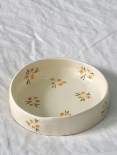 a white bowl with orange flowers on it sitting on a white tablecloth covered surface