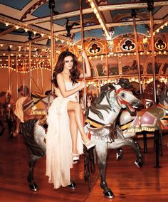 a woman sitting on top of a carousel next to a horse