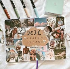 an open notebook with the words vision board surrounded by photos and pencils on a white sheet