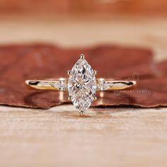 a pear shaped diamond engagement ring sitting on top of a wooden table next to a leaf