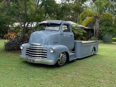 an old blue truck is parked on the grass in front of some trees and bushes