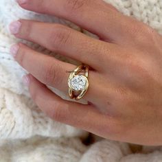 a woman's hand wearing a gold ring with a white diamond on the middle