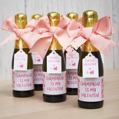 four bottles of champagne with pink bows and tags attached to the top, sitting on a table