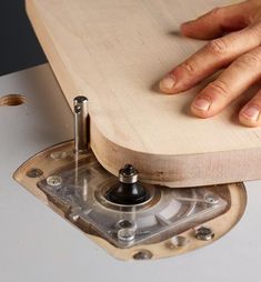 a person's hand on top of a piece of wood with a machine tool