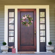 a front door with two planters and a wreath on it