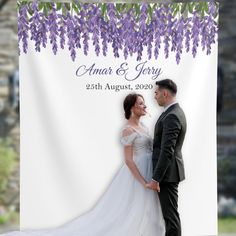 a couple standing next to each other in front of a purple flowered backdrop for their wedding