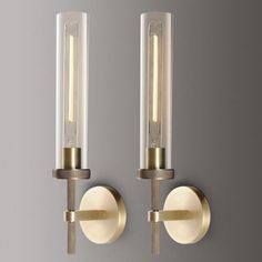 two light wall sconces with clear glass tubes on the back and gold trim