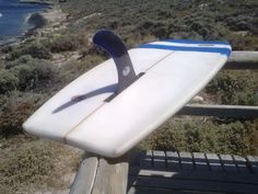 a white surfboard sitting on top of a wooden bench next to the ocean and grass