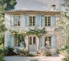 an old house with blue shutters on the front and side doors, surrounded by greenery