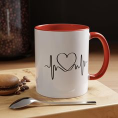 a red and white coffee mug sitting on top of a wooden table next to a spoon