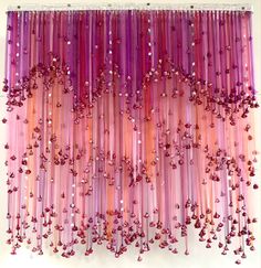 purple and pink streamers hanging from the ceiling in front of a white wall with red beads