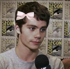 a young man with a pink bow on his head is talking to the camera while holding a microphone