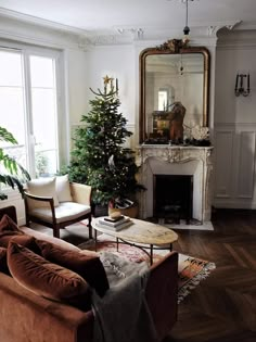 a living room filled with furniture and a fire place next to a christmas tree on top of a hard wood floor