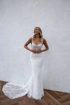 a woman in a white wedding dress standing on a wooden floor with her hands on her hips