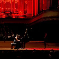 a person sitting at a piano in front of a stage with red lights on it