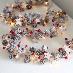 a wreath made out of pine cones and red berries on a white surface with christmas lights