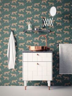 a bathroom with green and gold wallpaper, copper faucet, white cabinet and sink