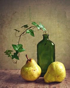 two pears and a green bottle on a wooden table with ivy growing out of it