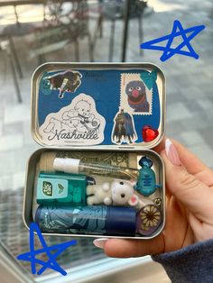 someone is holding an open tin with various items in it and there are blue stars above them