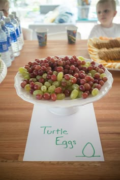 there is a cake with grapes on it and a little boy in the background looking at it