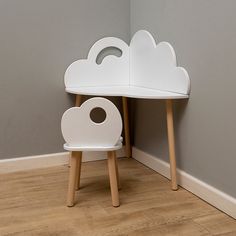 a small white table and chair with a cloud shaped shelf on the top, in front of a gray wall