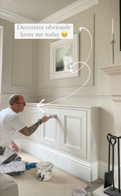 a man is painting the wall in his living room with white paint and an emoticive message