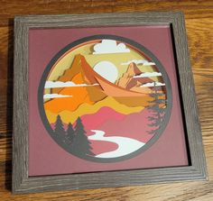 a wooden frame with an image of mountains and trees in the center on a wood table