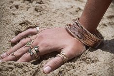 a woman's hand with bracelets and rings in the sand