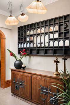 a vase with flowers sitting on top of a wooden cabinet next to two lamps hanging from the ceiling