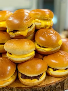 a pile of mini burgers sitting on top of a wooden board covered in cheese