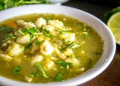 a white bowl filled with soup and garnished with cilantro, parsley and lime