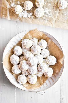 a plate full of snowball cookies on top of a wooden table next to a napkin