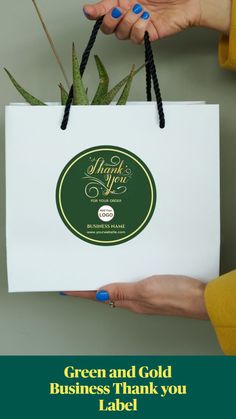 a person holding a white bag with green and gold stickers on it that says thank you