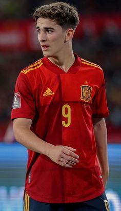 a young man wearing a red shirt and blue shorts standing in front of a soccer ball