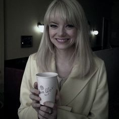 a woman in a yellow coat holding a coffee cup with the words ugly on it